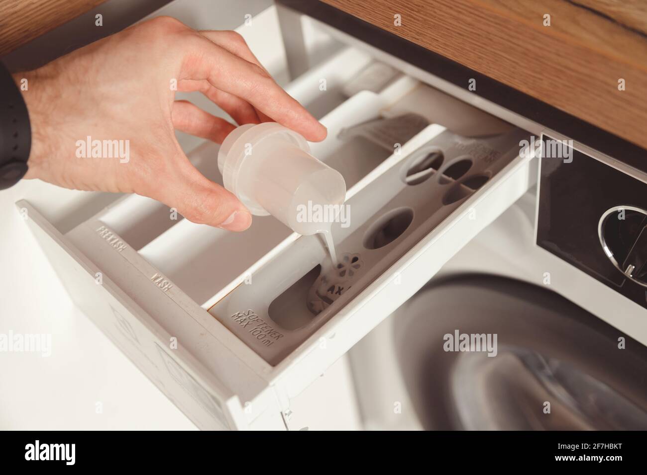 Man pouring the washing fabric conditioner into the washing machine to get more softer clothes Stock Photo