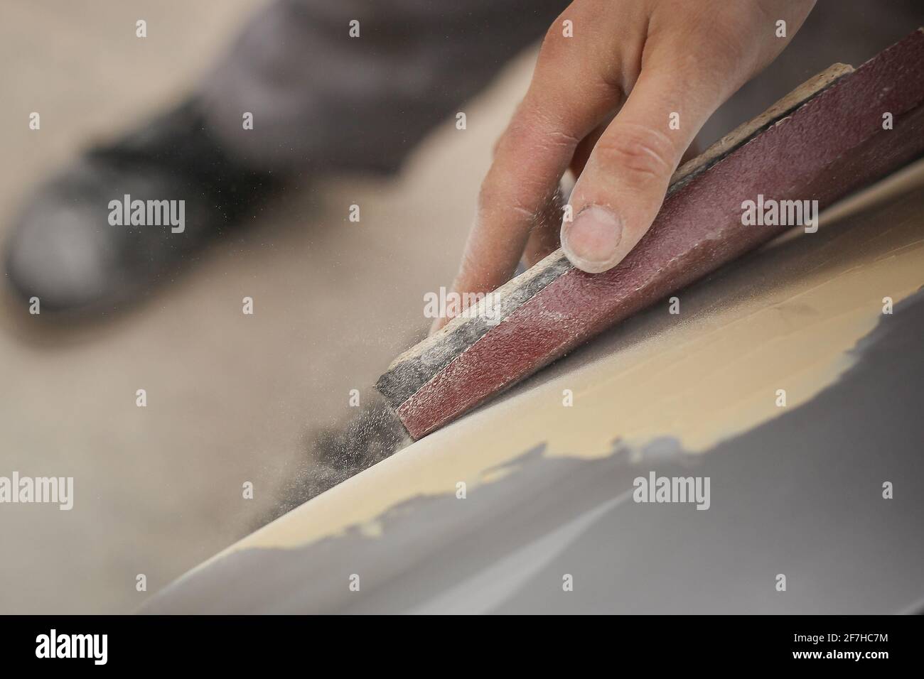 A hand of a man is seen sanding an old vintage car using a block of wood and brown sand grit paper. Manual dry sanding of a car in restoration, a proc Stock Photo