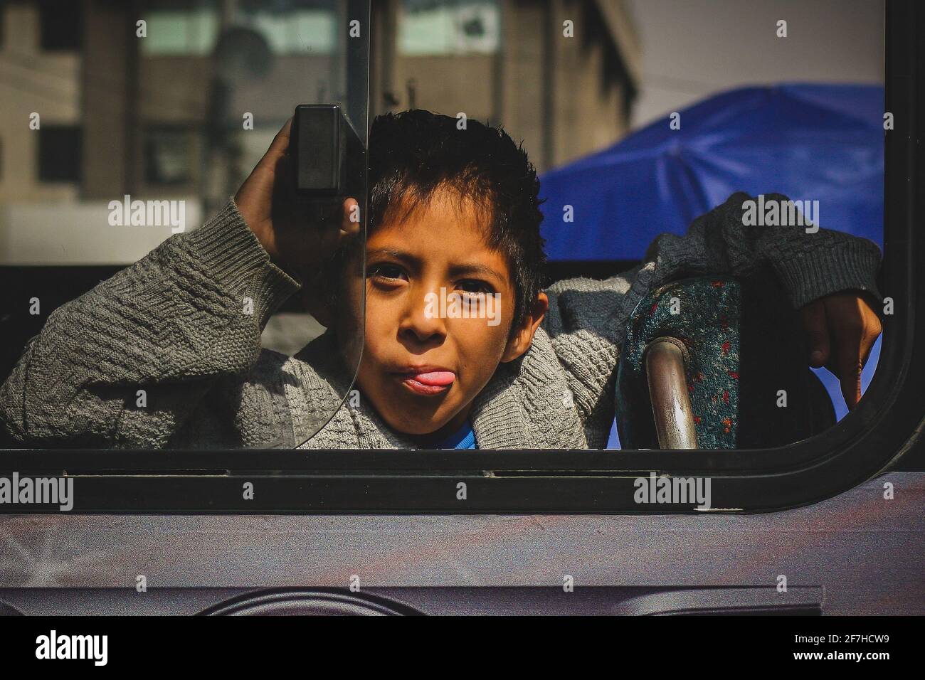 MEXICO CITY, MEXICO, 21.1.2012: Mexican kid showing his toungue from a local bus in the city. Nosy kid showing his tongue Stock Photo