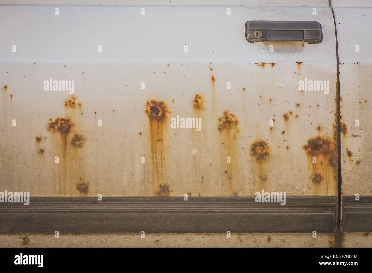 Brown rust patches on a white door of a passenger car. Rust eating through a driver door of a