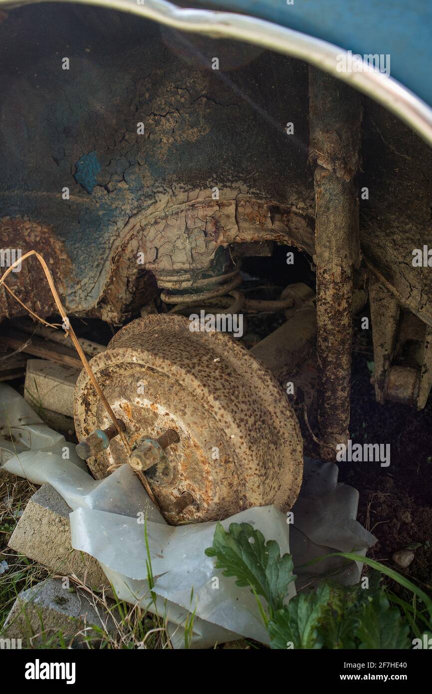 Heavily rusted drum brakes or exterior of brake drum with coil spring and rear axle on an abandoned vintage vehicle. A wheel is missing on an old blue Stock Photo