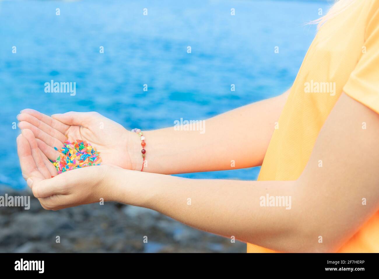 Hands full of microplastics on the beach. Different plastic colored