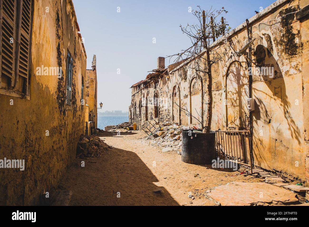 One of the less atractive streets on the famous slave island of Goree. Row of houses with dirt and trash on the ground. City of Dakar is seen in the b Stock Photo