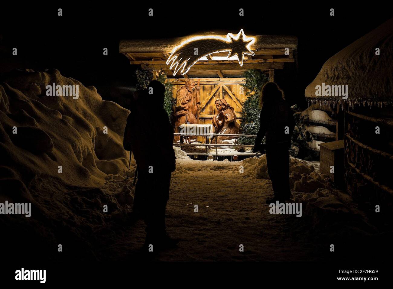 People admiring a baby jesus in a crib, as part of an outdoor festive display during a snowy night. Stock Photo