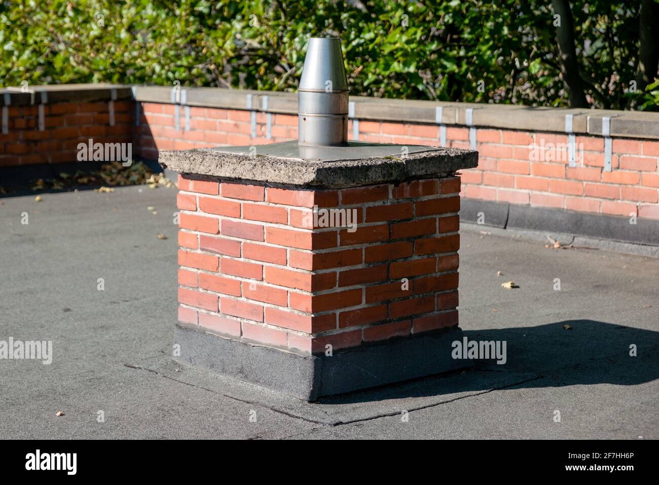 The round, metal vertical flue of an industrial commercial boiler central heating system on top of a flat roof Stock Photo