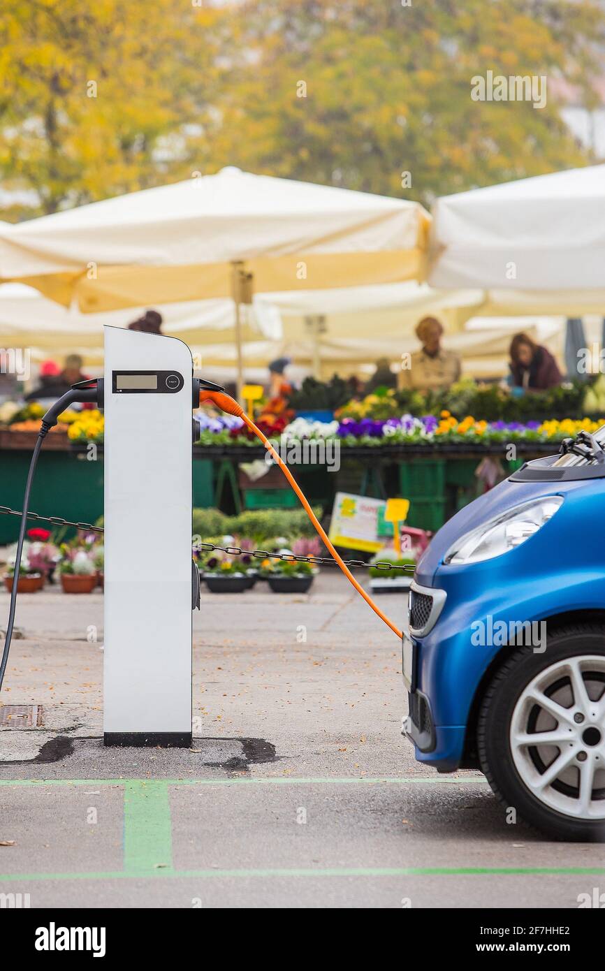 Electric car being charged in front of a flower shop. Concept of green energy with conserving nature. Electric car and flowers in the background. Ecol Stock Photo