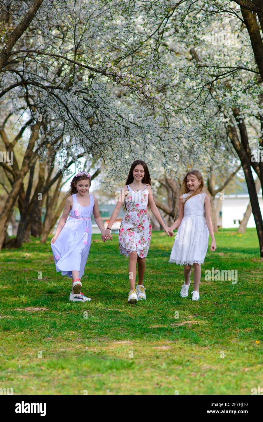 Three adorable girls in dresses hold hands in a circle holding hands ...