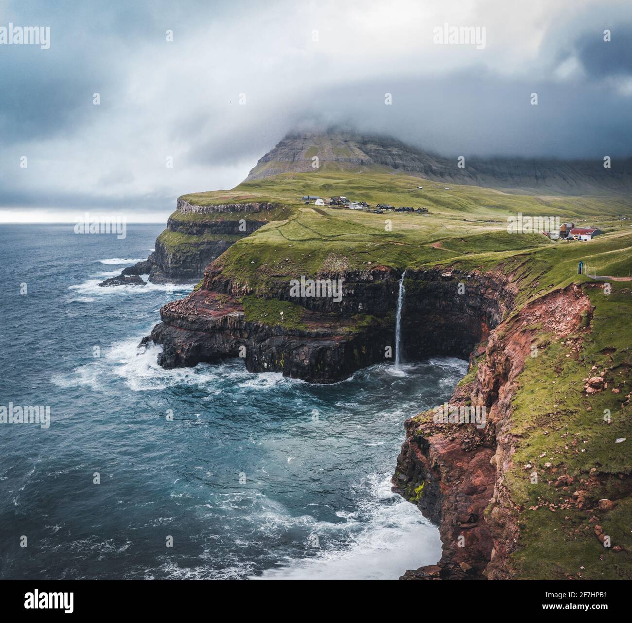 Aerial drone view of Gasadalur village and Mulafossur its iconic waterfall, Vagar, Faroe Islands, Denmark. Rough see in the north atlantic ocean. Lush Stock Photo