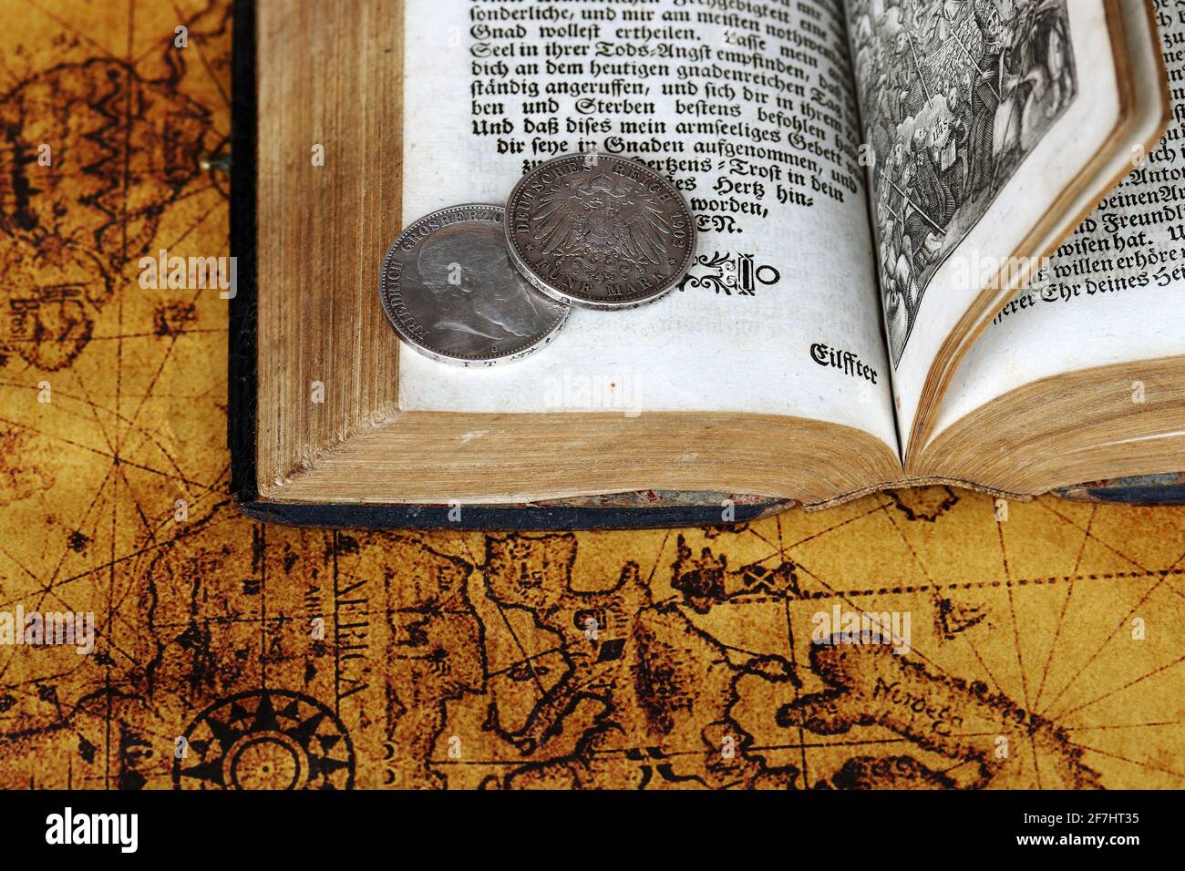Old silver coins from 1902 and an antique book from 1763 on a world map Stock Photo