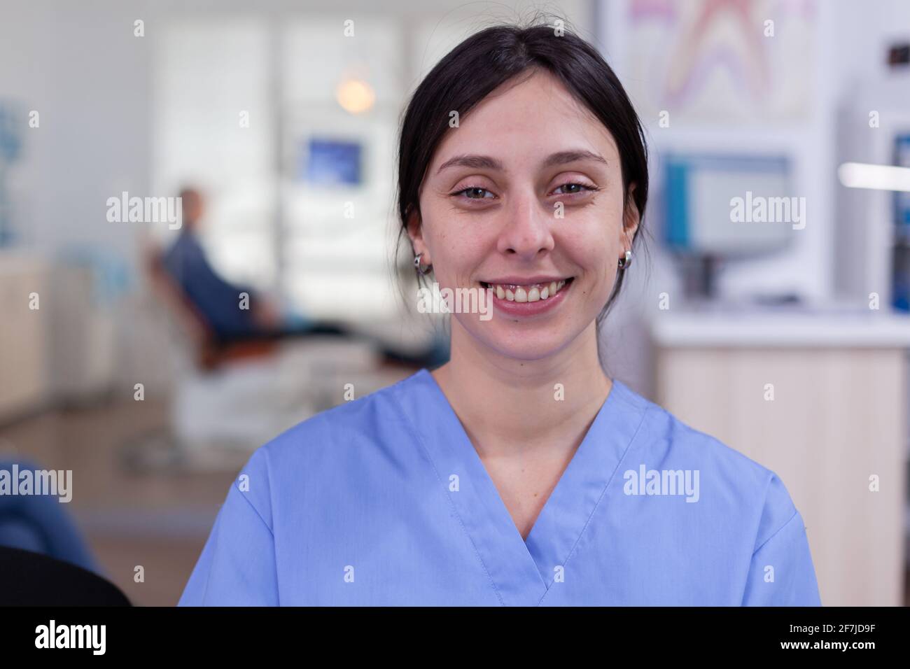 Smiling stomatology nurse looking at camera in dentist office wainting area, senior man waiting for teeth health examination. Dentistiry woman sitting on chair. Stock Photo