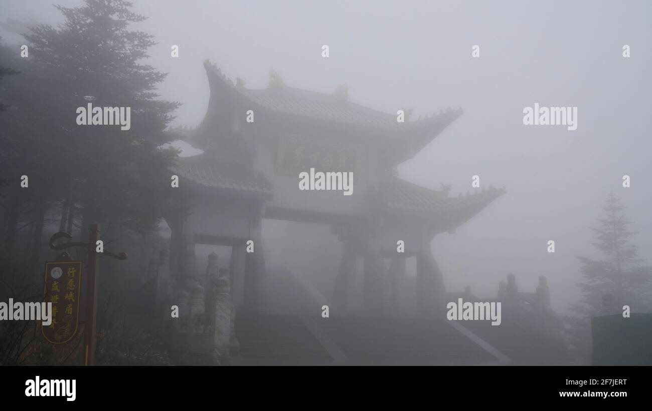 A memorial gate barely visible in heavy fog of Mount Emei. Stock Photo