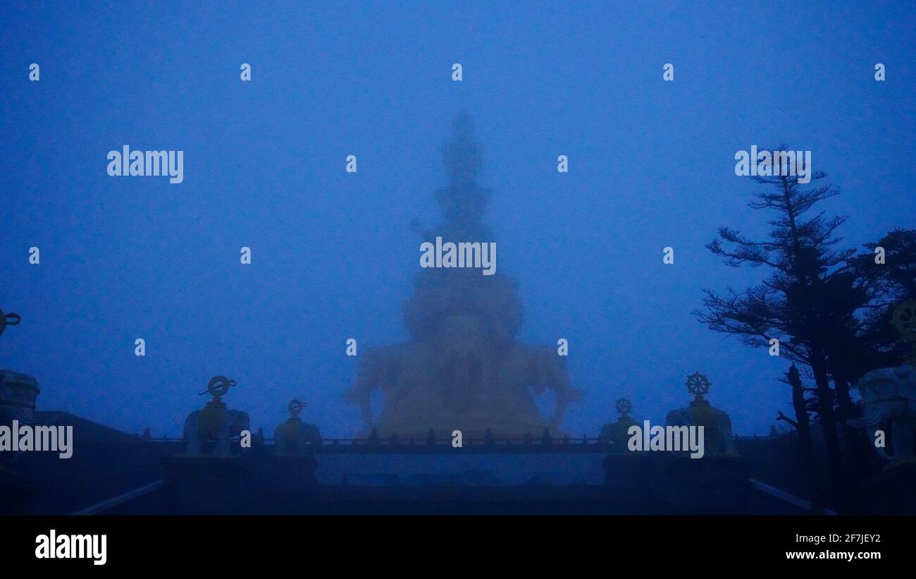 A golden buddha statues barely visible in the heavy morning fog on top of Mount Emei in Szechwan, China. Stock Photo