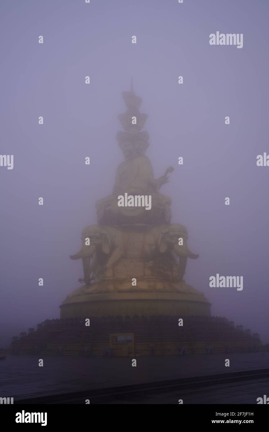 A golden buddha statues barely visible in the heavy morning fog on top of Mount Emei in Szechwan, China. Stock Photo