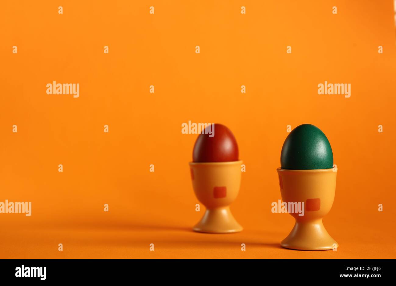 Two easter colored painted traditionally eggs into eggcups clsoe up on orange background. Stock Photo