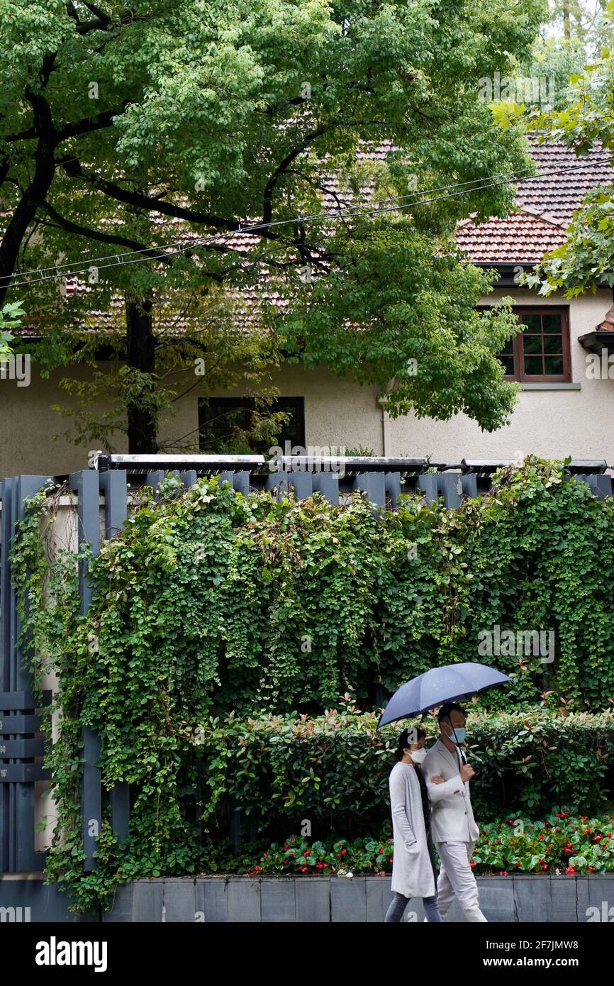 Two peple with face mask on waling on streen with green trees and old house in Wukang Road of Shanghai city. Stock Photo