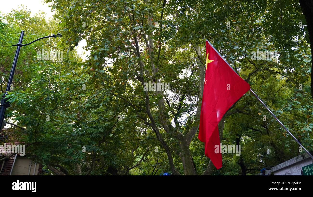 China National flag hanging to celebrate National Holiday with green trees in Shanghai city. Stock Photo
