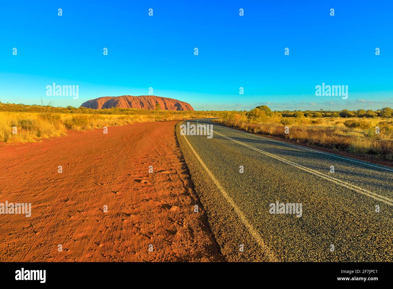 Road leading to Uluru Ayers Rock at vibrant color of sunset. The huge sandstone monolith icon of Australian outback in Uluru-Kata Tjuta National Park Stock Photo