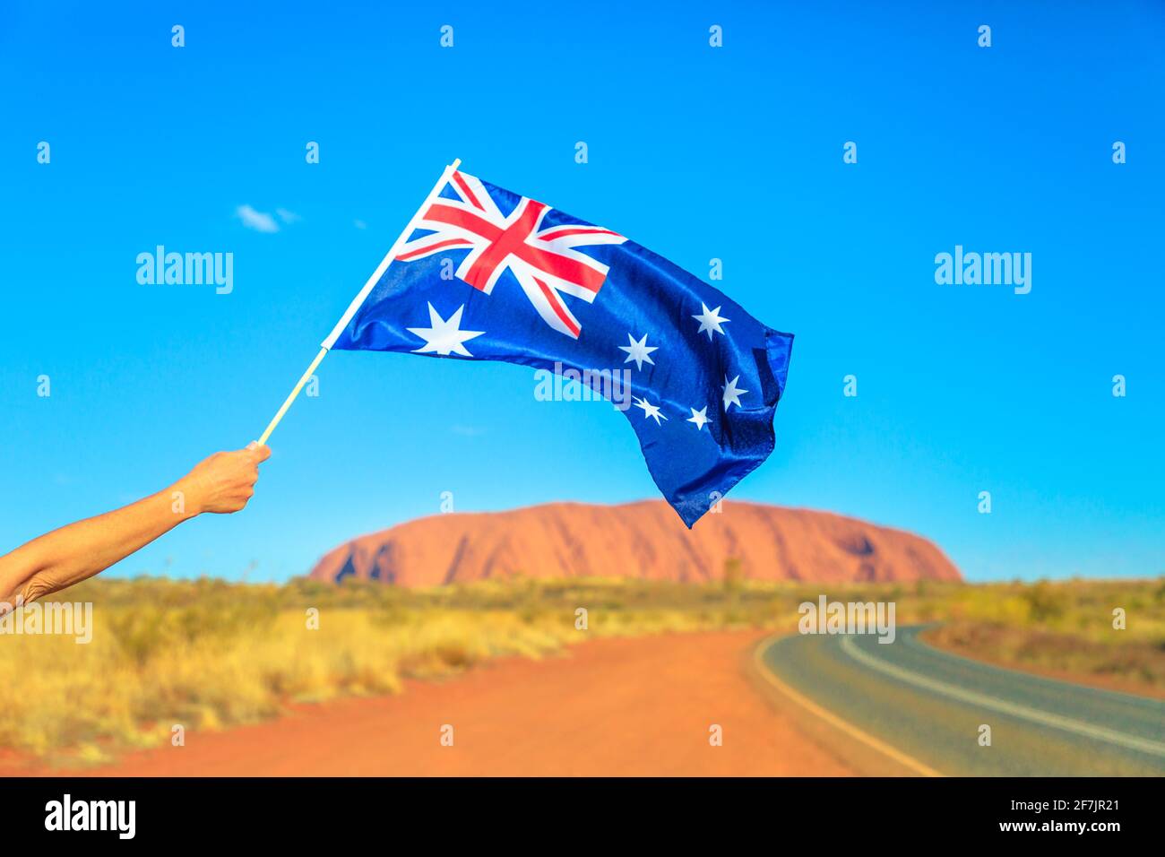 Woman's hand waving an Australian flag Red Centre Outback. Tourism in Northern Territory, Central Australia. Uluru Ayers Rock in Uluru-Kata Tjuta Stock Photo