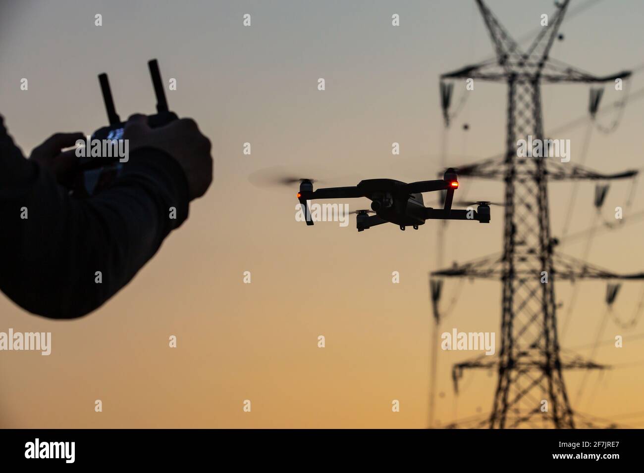 A concept of a man flying a drone collecting a data remotely from a power tower station or for telecommunication. Drone safety, power lines. Stock Photo