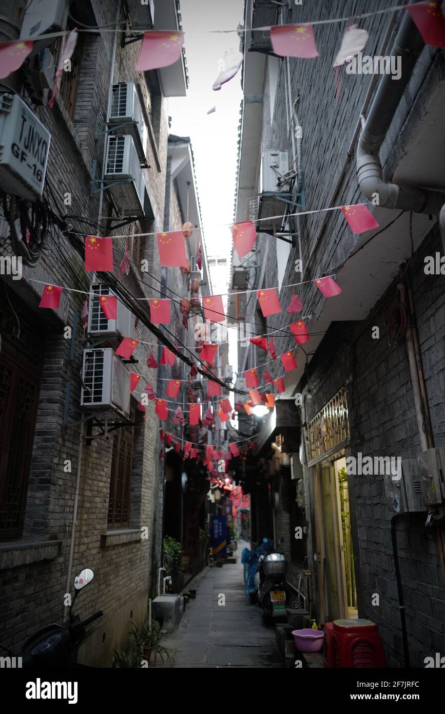 Small red flags are hanging above narrow alley with old houses. Stock Photo