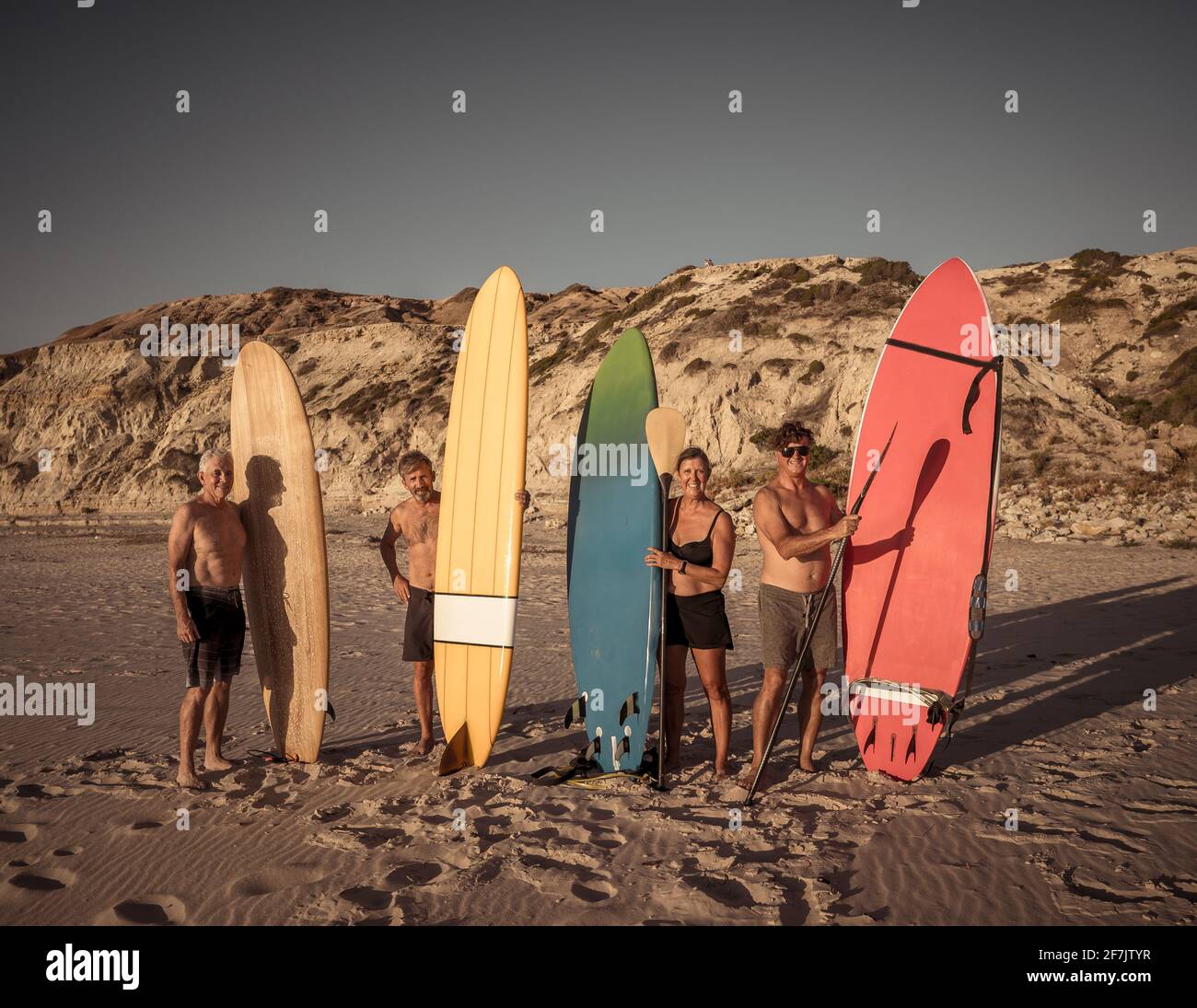 Group of senior surfers, woman and men, holding their colorful surfboards on remote beach. Mature retired friends enjoying surfing and outdoors lifest Stock Photo