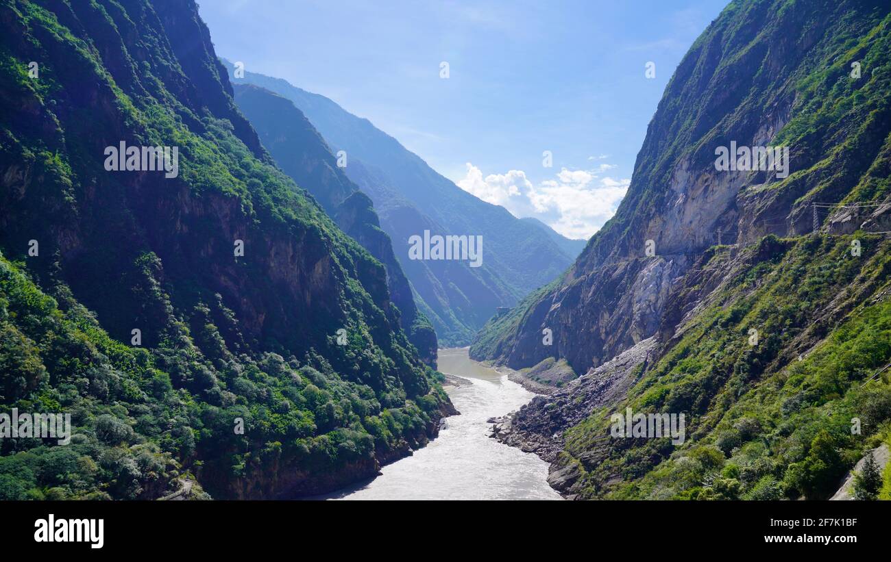 A river is running between valley with green mountains at both sides, and blue sky above, in Tiger Leaping Gorge of Lijiang. Stock Photo