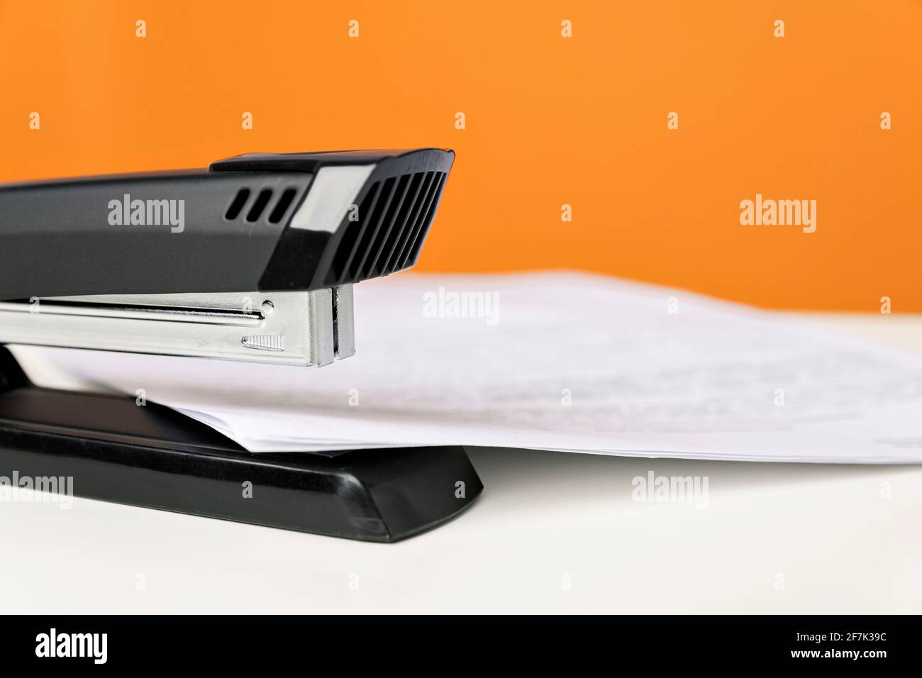Stapler on white table against bright orange background. Minimalistic, vivid colors. Office supplies. Stock Photo