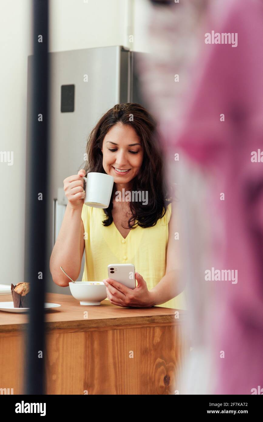 Woman talking on the phone while having breakfast in the kitchen at home Stock Photo