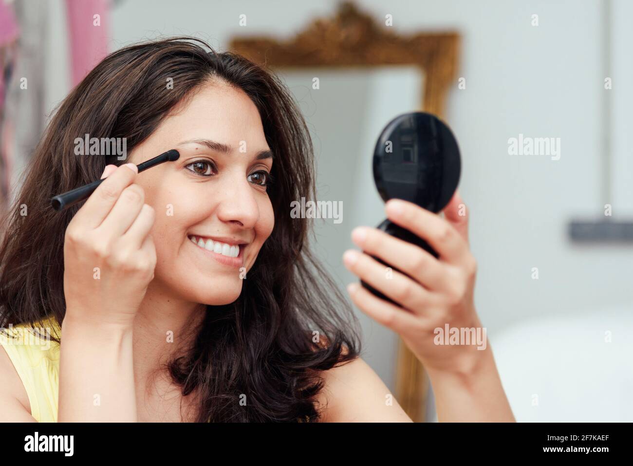 Young Latina putting on makeup in front of the mirror with her eye line pencil Stock Photo