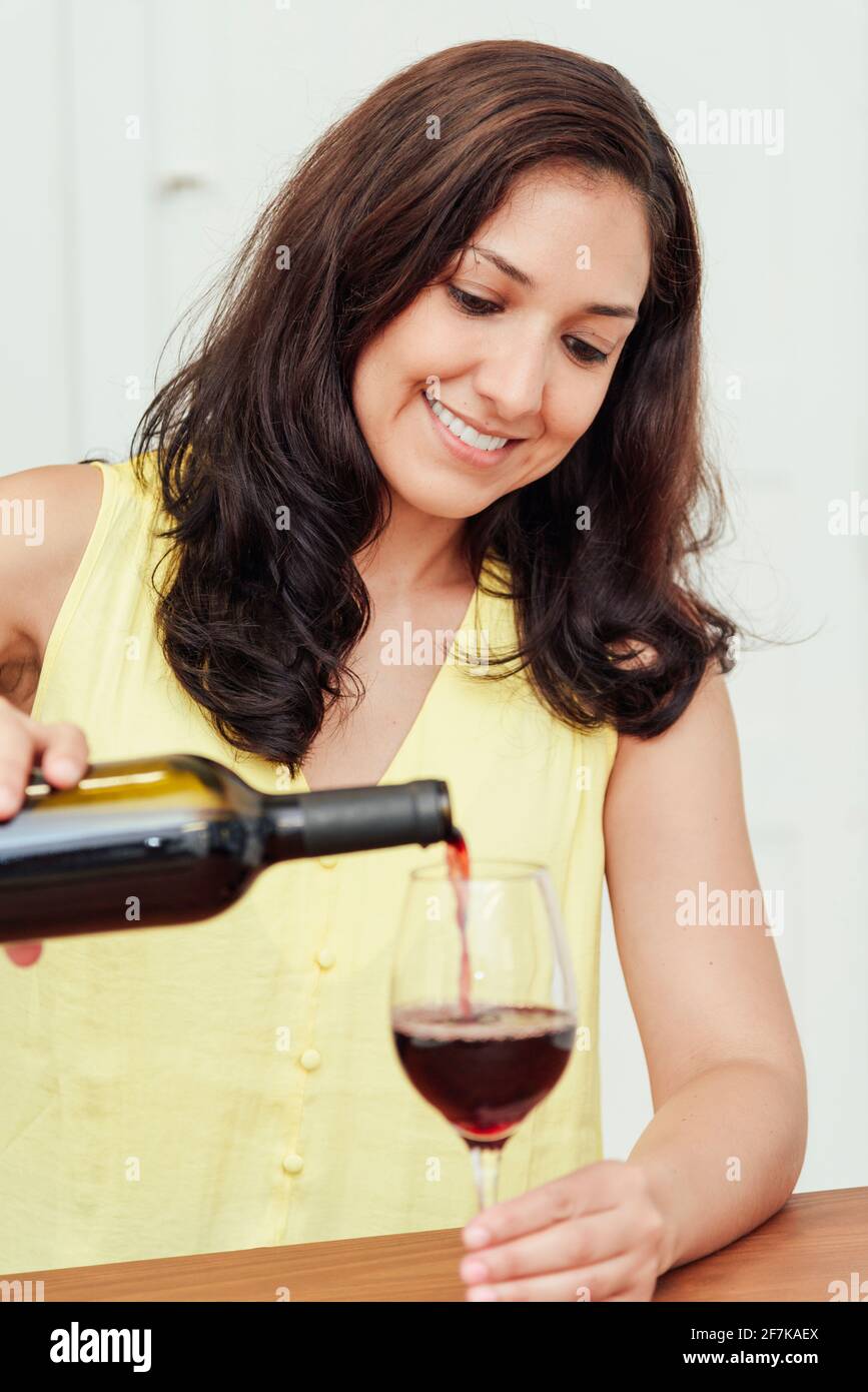 Young woman serving a glass of wine in the kitchen at home. Stock Photo