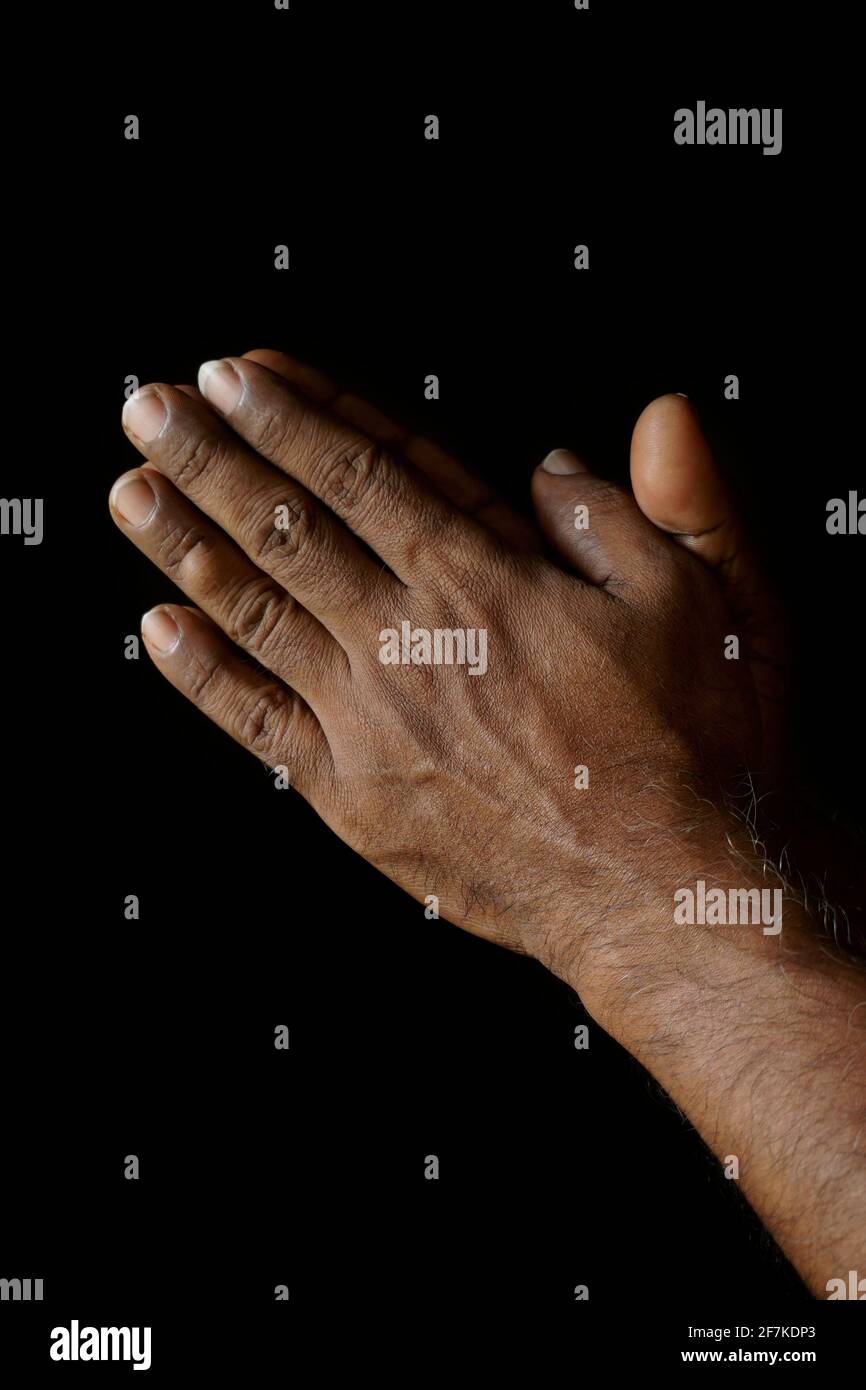 Praying hands of Indian Catholic man isolated on a black background. Stock Photo