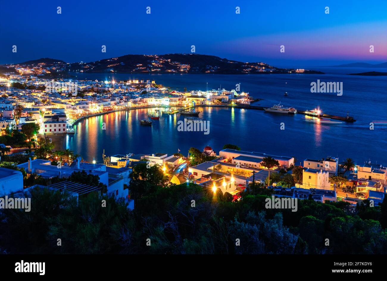 Beautiful night view of Mykonos, Greece, ships, port, whitewashed houses. Town lights up. Vacations, leisure, nightlife, Mediterranean lifestyle Stock Photo
