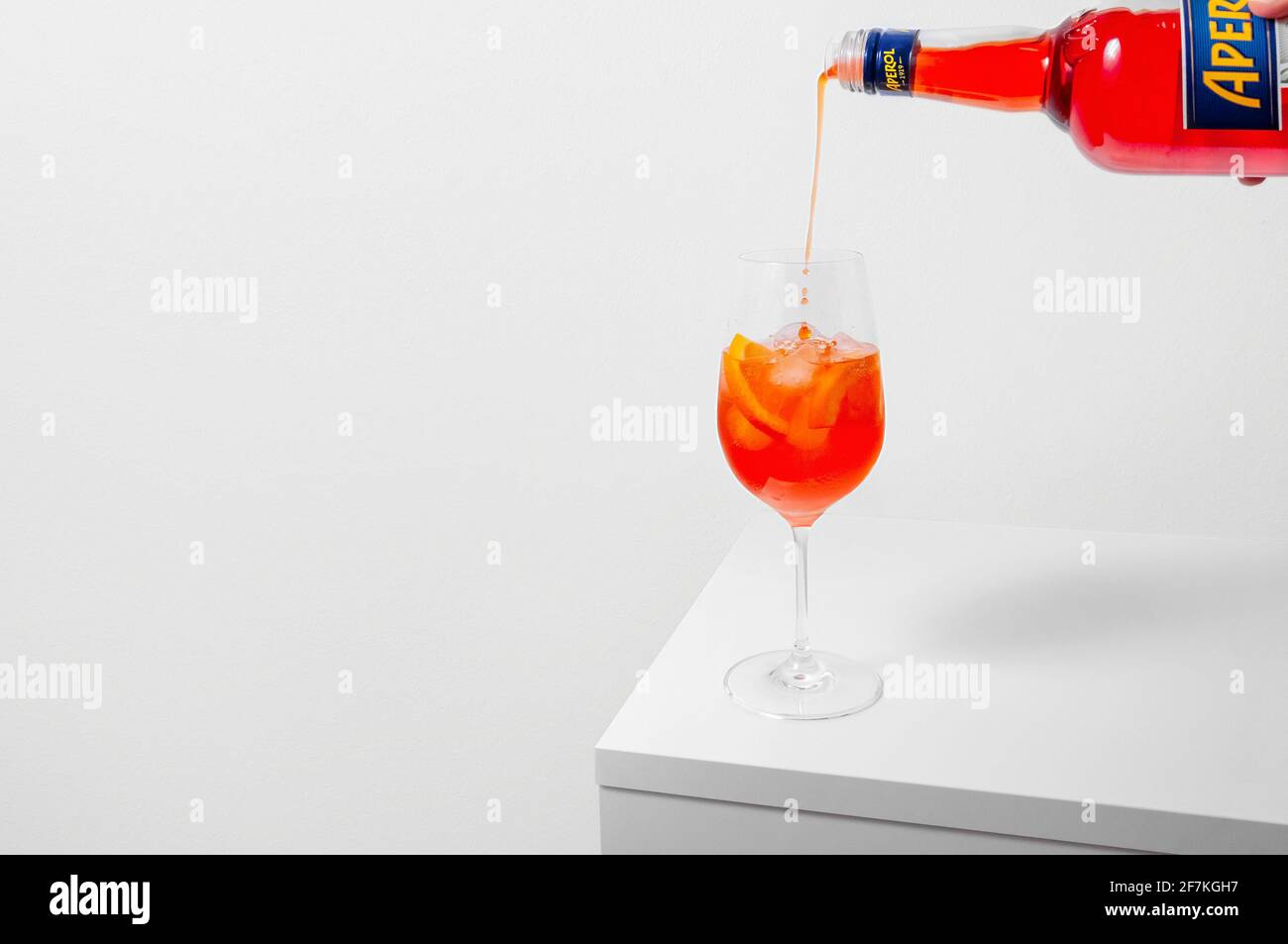 Lugansk, Ukraine - March 29, 2021: Aperol Spritz Cocktail. Pouring aperol in wine glass with ice on white background. Long fizzy drink. Minimal creati Stock Photo
