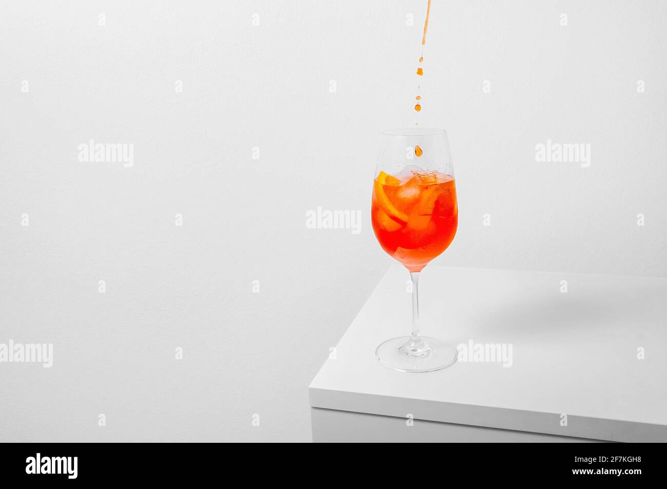 Aperol Spritz Cocktail. Pouring aperol in wine glass with ice on white background. Long fizzy drink. Minimal creative concept. Stock Photo