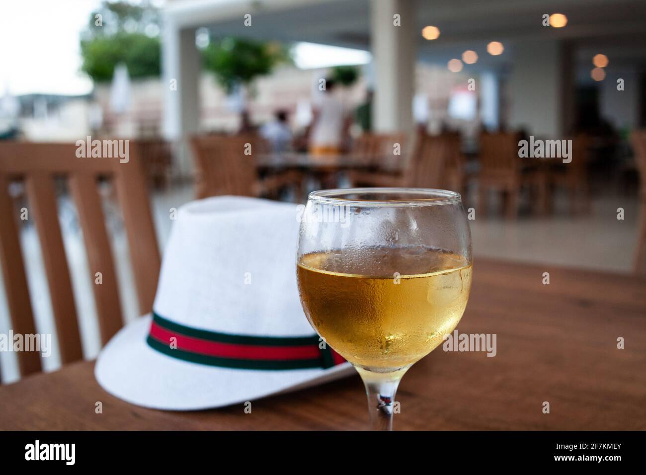 A glass of white wine and white hat on table. Condensation on the glass of refreshing wine. Cool drink in open-air restaurant. Relax with alcohol drin Stock Photo