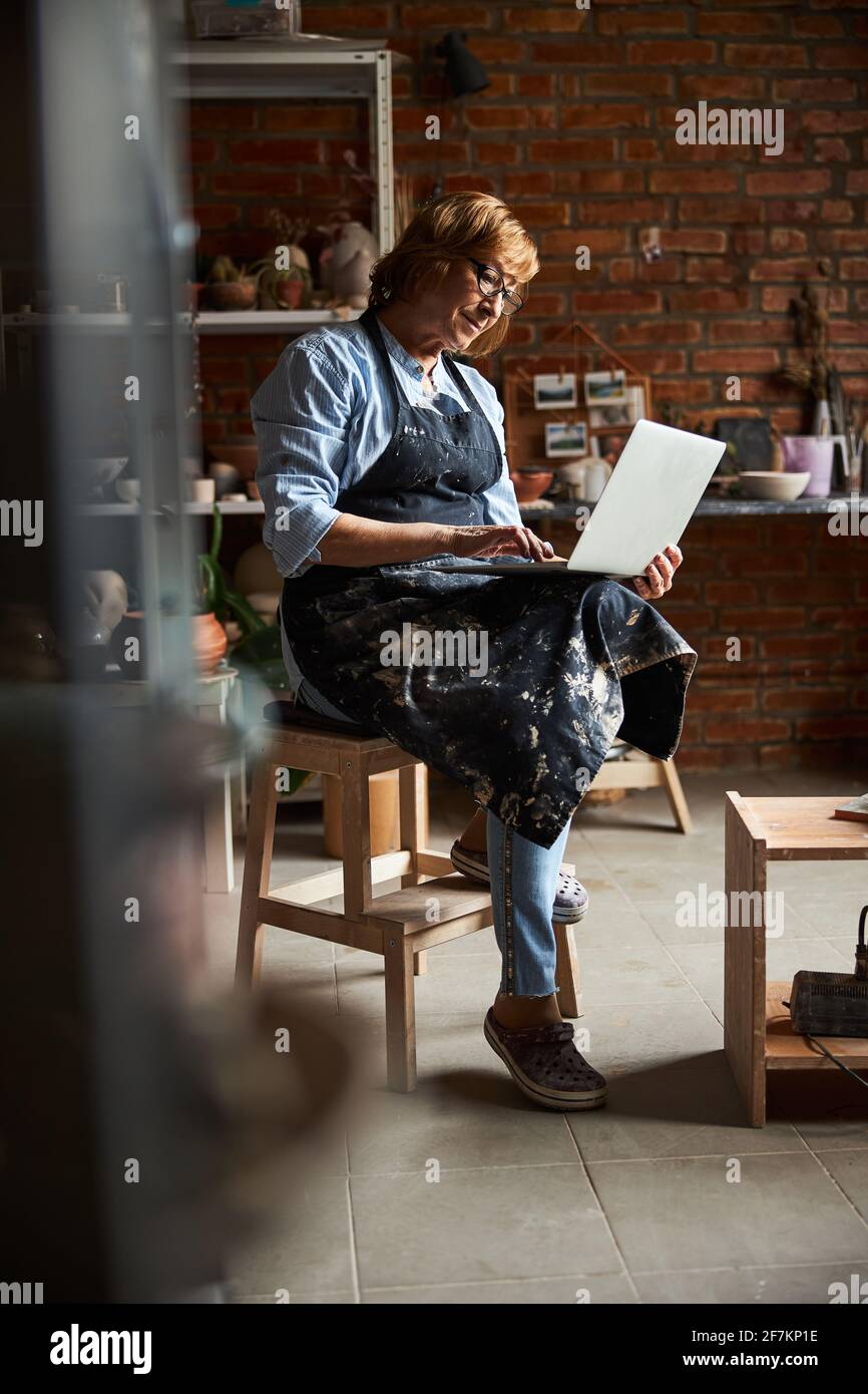 Nice senior woman using notebook in pottery workshop Stock Photo