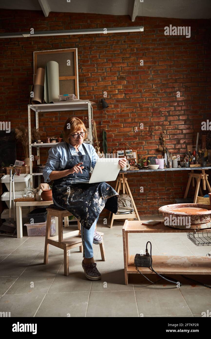 Nice female potter using notebook in pottery workshop Stock Photo