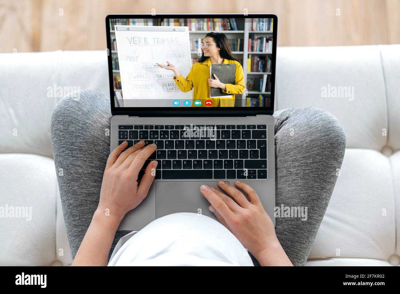 Online training during pregnancy. A pregnant woman holds a laptop while sitting on the couch, is listening an online lecture, on the laptop screen a clever teacher shows information during video call Stock Photo