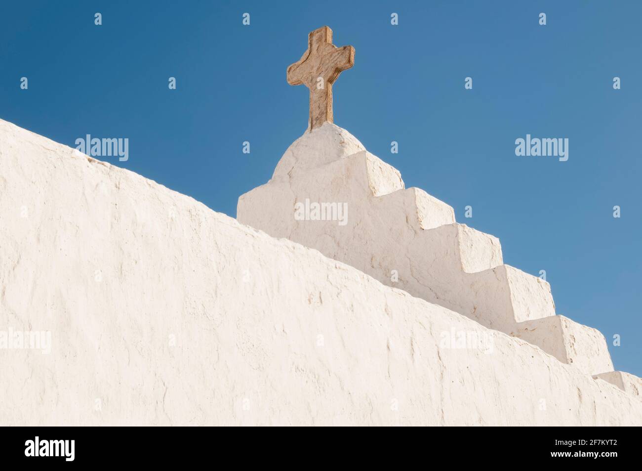 Close-up of a white roof, the exterior of a church with a stone cross, Greece, Cyclades Islands, Mykonos. Blue sky in the background. Concept travel Stock Photo