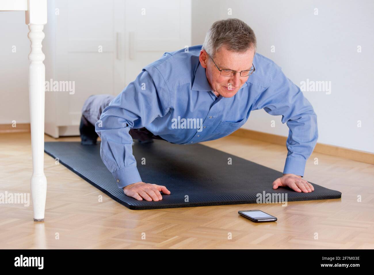 Mature businessman doing push ups at home - selective focus on the face Stock Photo