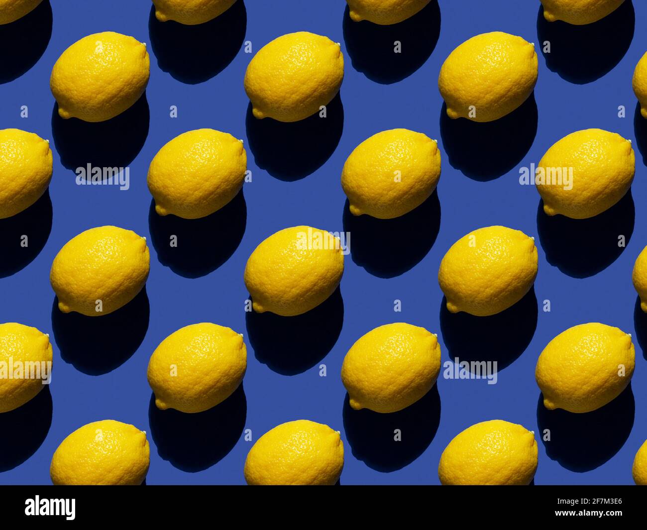 Rhythmic pattern of lemons on a blue background. Hard shadows. Stock Photo