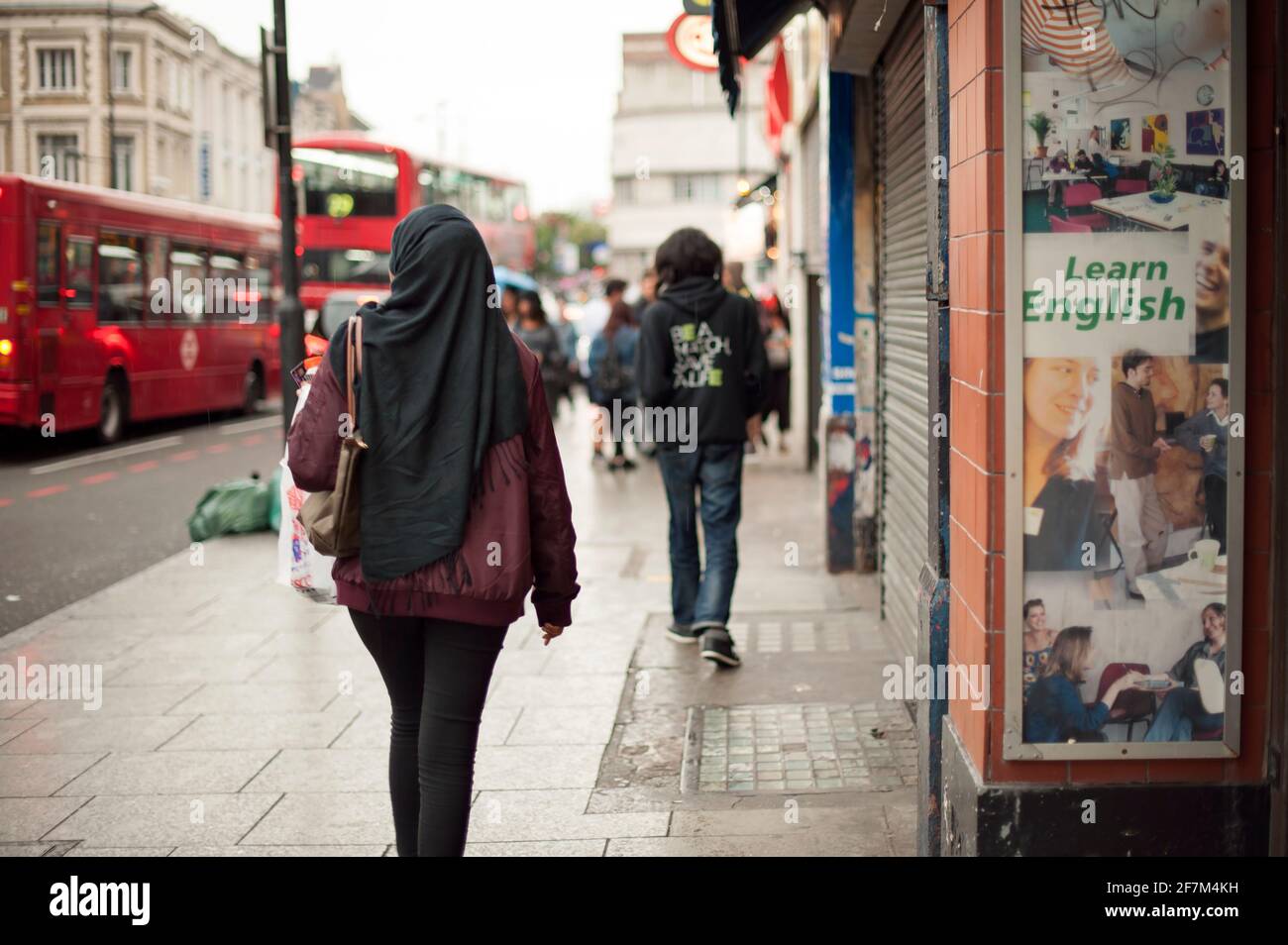 Rear view of muslim woman in hijab passing by a 'Learn English' advert. Camden High Street, London, UK. Aug 2015 Stock Photo