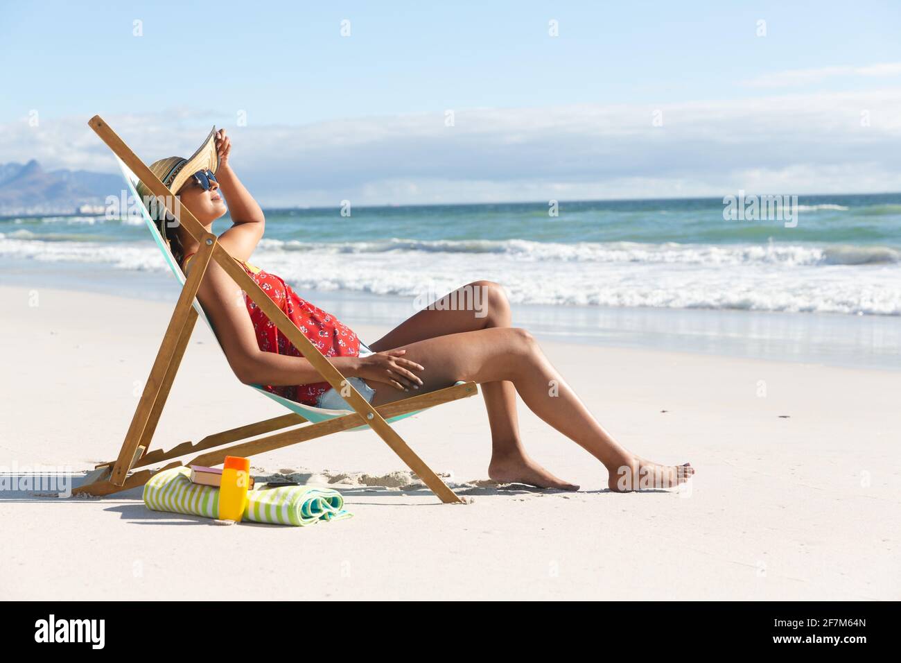 Mixed race woman on beach holiday sitting in deckchair sunbathing Stock Photo