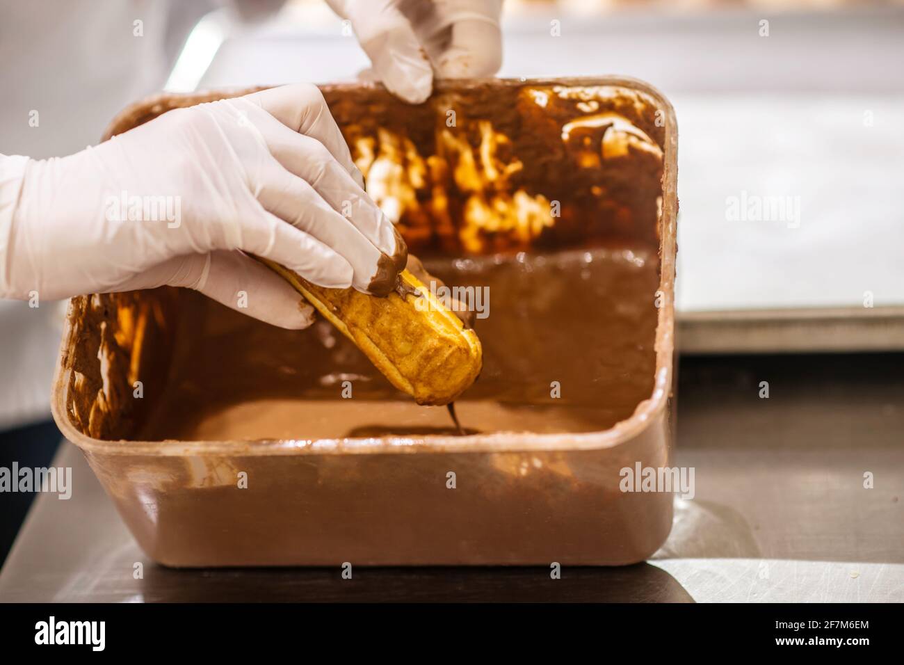 Hands dipping eclair in chocolate fondant in tray Stock Photo Alamy