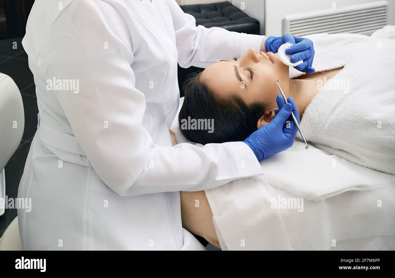 Beautician using comedone extraction tool to clean the woman's face