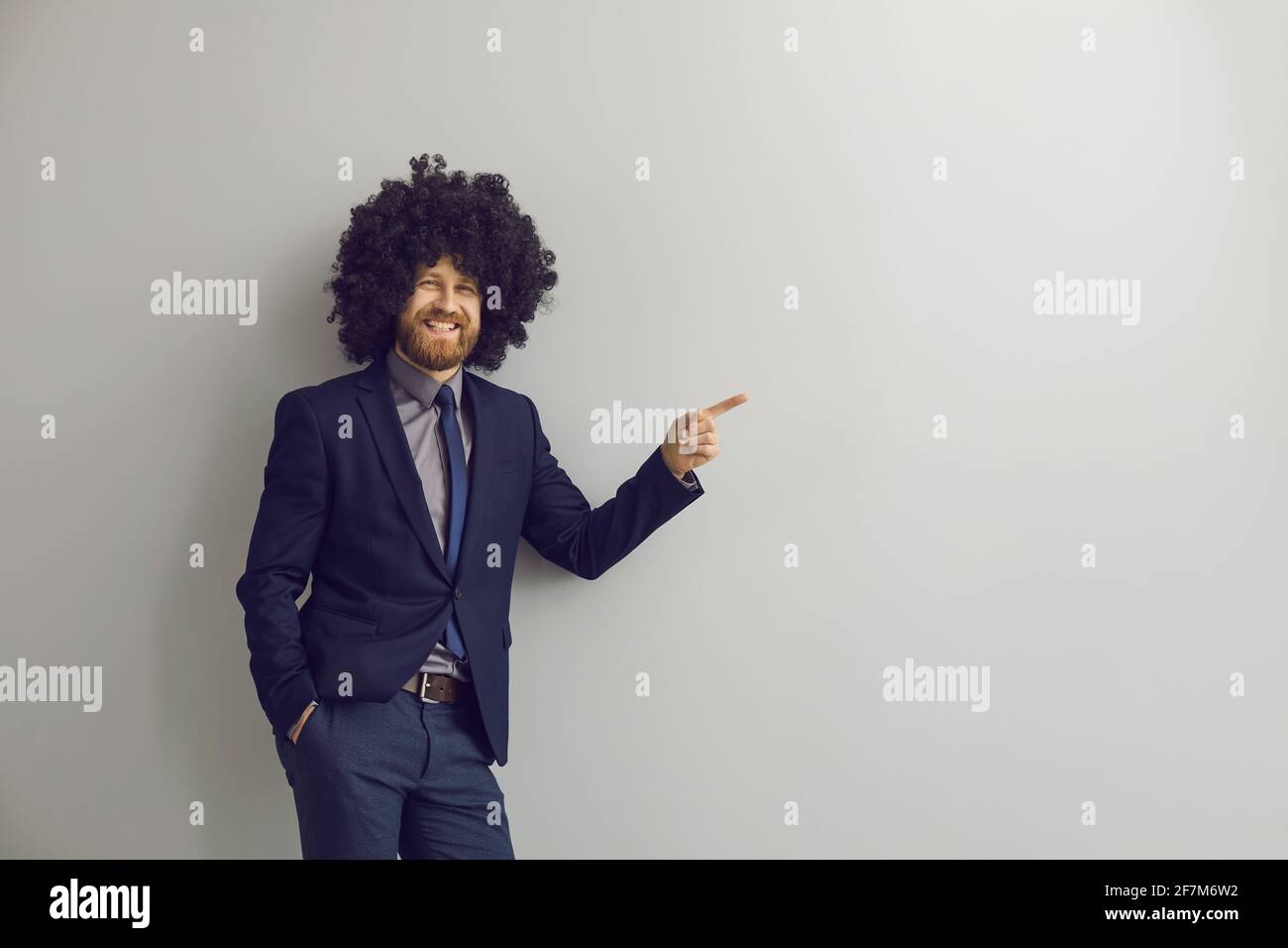Loudly laughing business man in funny afro curly hair wig pointing at something Stock Photo