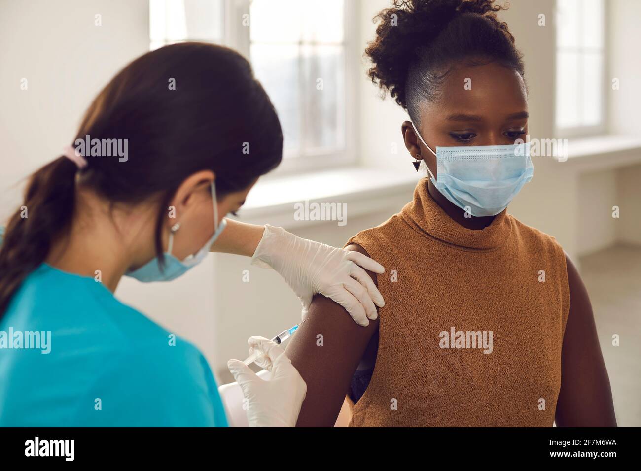 African american woman patient in protective face mask sitting getting vaccination injection Stock Photo