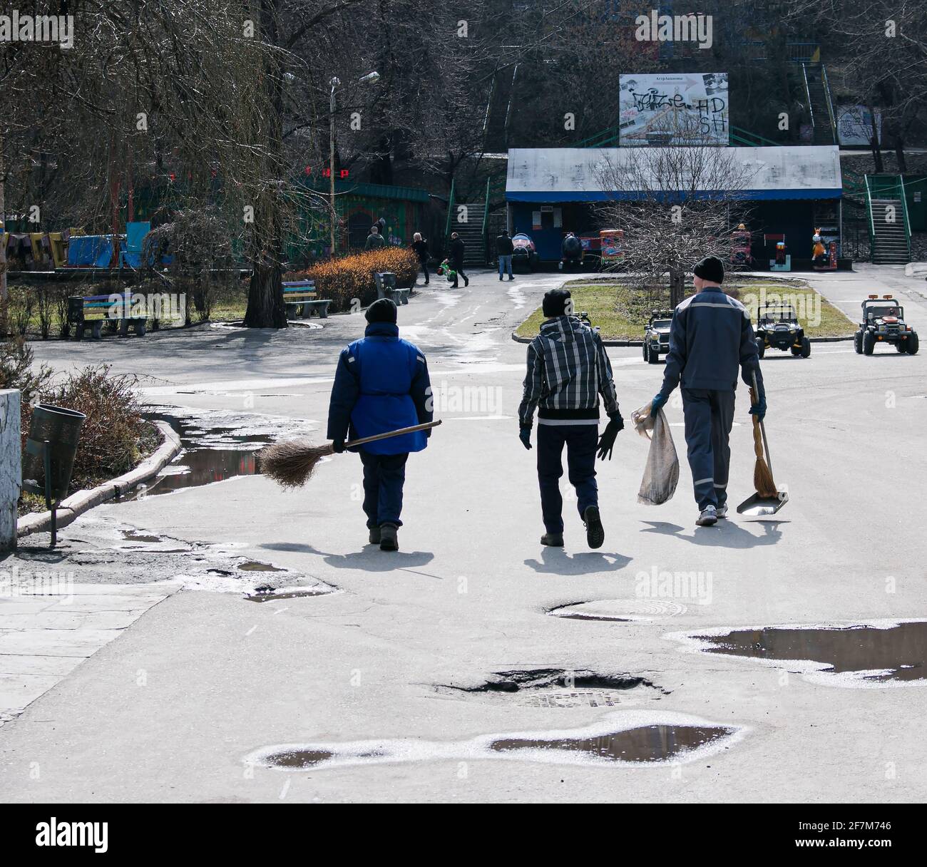 Municipal service workers carry brooms and shovels. Workers cleaned the park after winter. Stock Photo