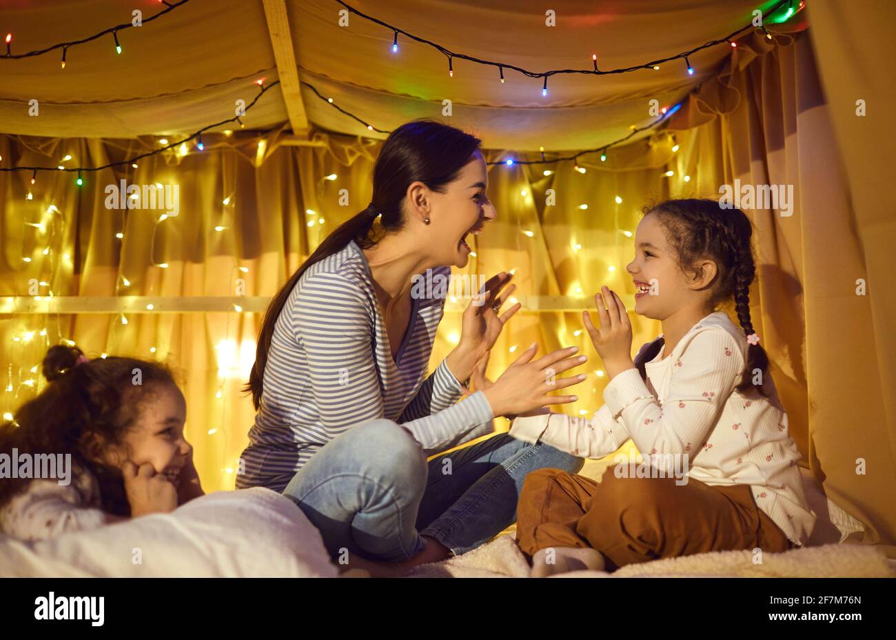 Happy mother playing with adorable cheerful children in home tent at evening Stock Photo