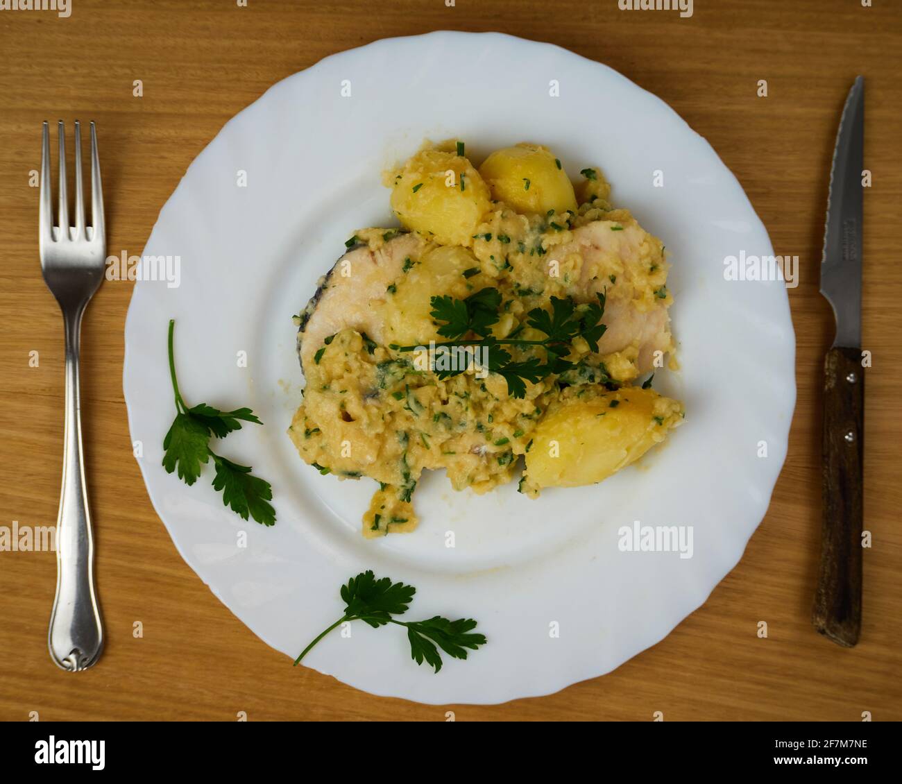 Hake served on a green sauce with parsley leaves in a white dish with cutlery. Top View Stock Photo